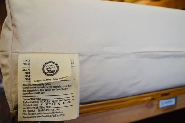 Holy Lamb Organics wool and latex mattress, 6.5 inch thick, showing a close-up of the mattress tag and textured fabric surface.