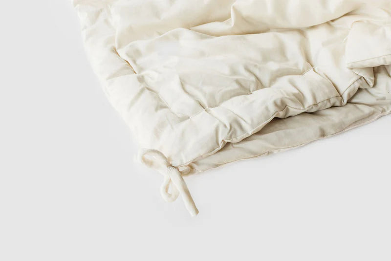 Holy Lamb Organics all-season wool comforter draped over a bed, showing its cozy, soft fabric and plush texture.