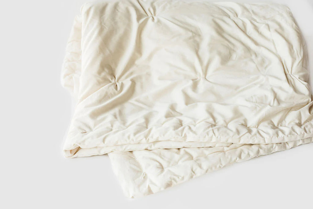 Cream-colored Holy Lamb Organics certified organic wool comforter spread neatly on a bed with cozy pillows.
