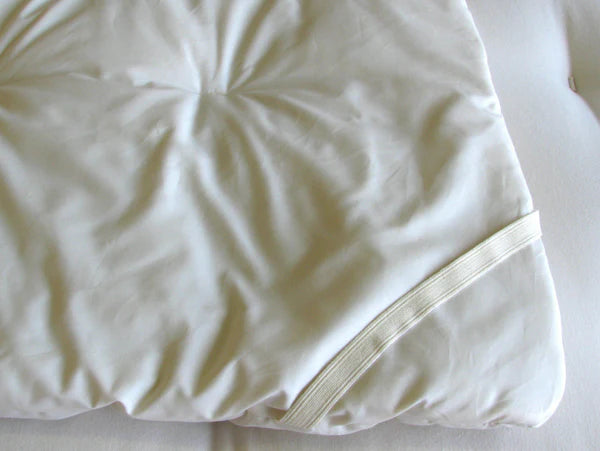 Organic crib mattress topper for babies by Holy Lamb Organics, showing plush, eco-friendly bedding with secure straps for safety.
